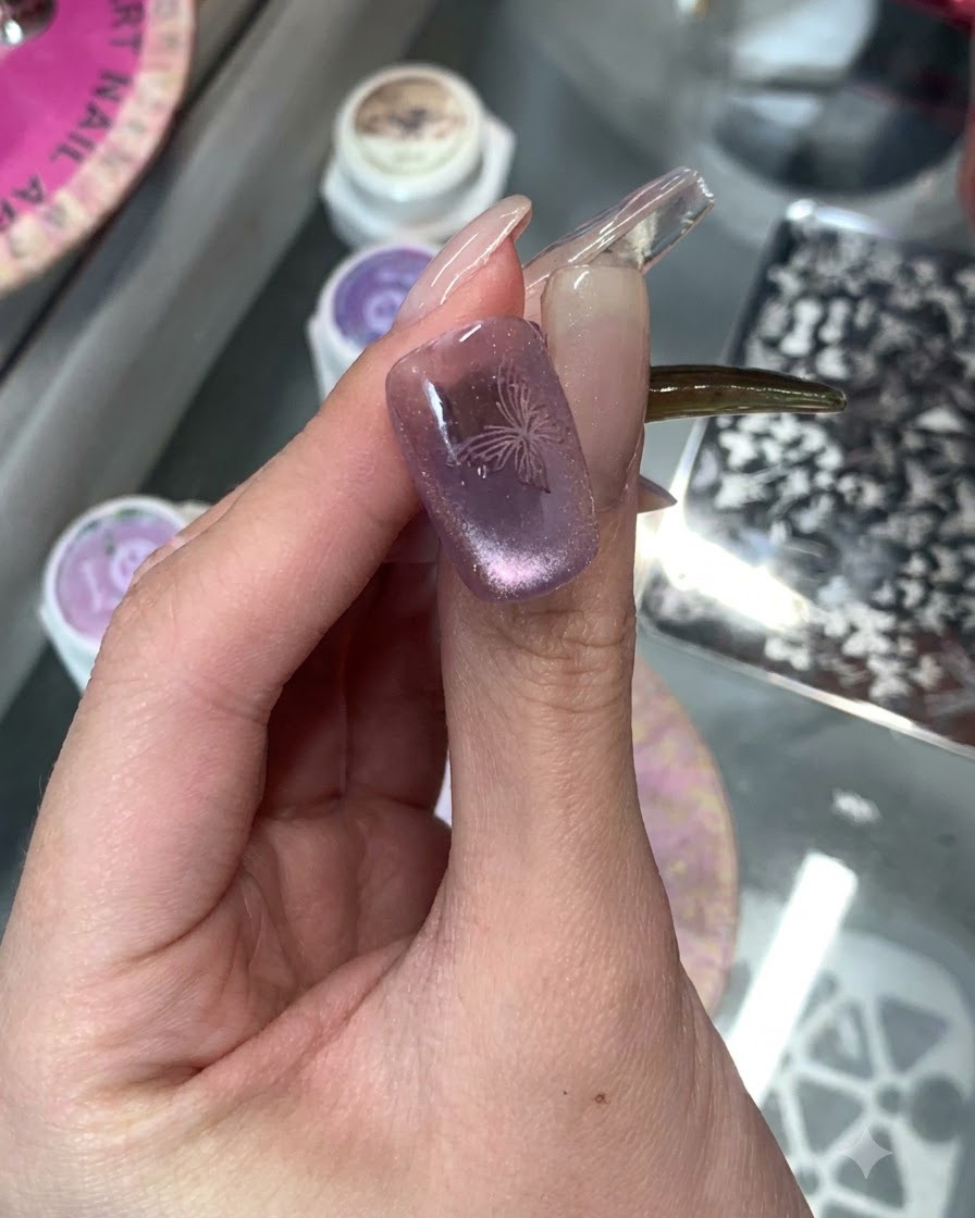 Primo piano di ununghia viola cat-eye con un delicato design a farfalla stampato sopra.