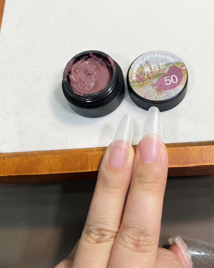 Un pennello che trattiene una piccola quantità di gel solido rosa bean paste vicino alla punta di unestensione per unghie trasparente.