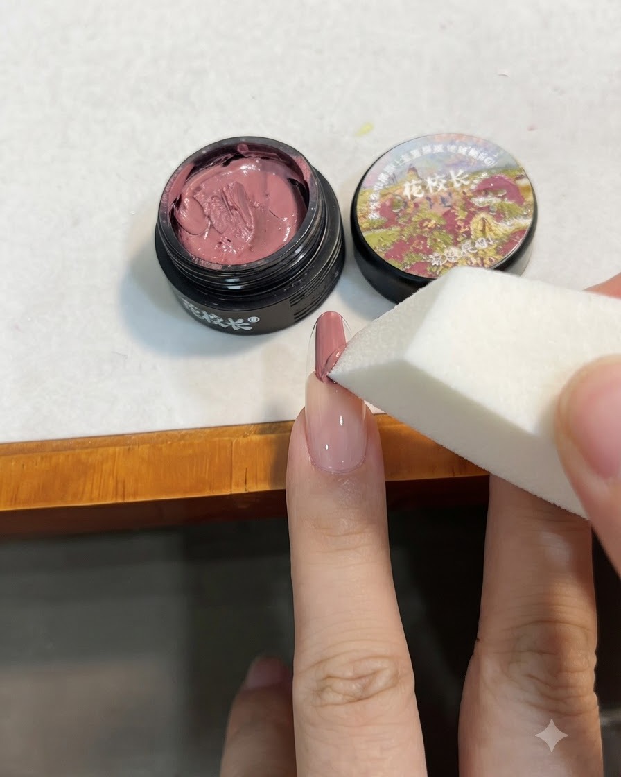 Una spugnetta da trucco bianca che tampona il gel rosa sullunghia per sfumarlo verso il basso in una sfumatura.