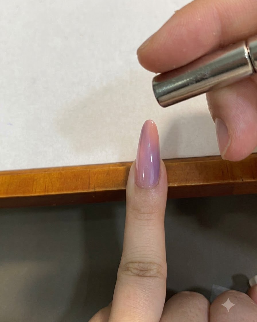 Un piccolo magnete tenuto vicino sopra ununghia cat-eye sfumata rosa per modellare il pigmento magnetico.