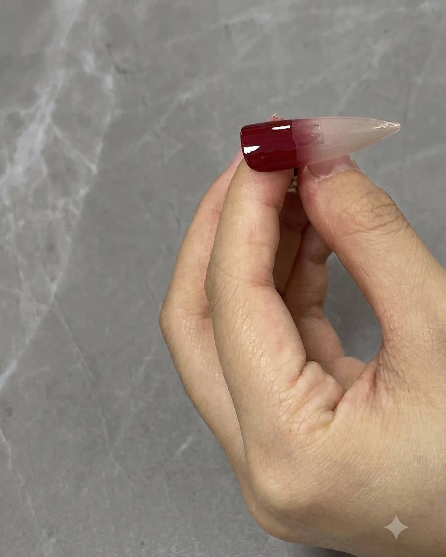 Un primo piano di un pennello per unghie che sfuma un gradiente rosso vino verso il basso su una tip neutra.