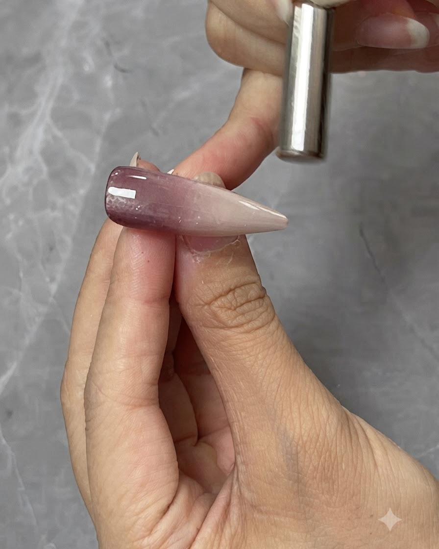 Un magnete cilindrico tenuto vicino sopra una tip per unghie in gel cat-eye per modellare il riflesso di luce magnetico.