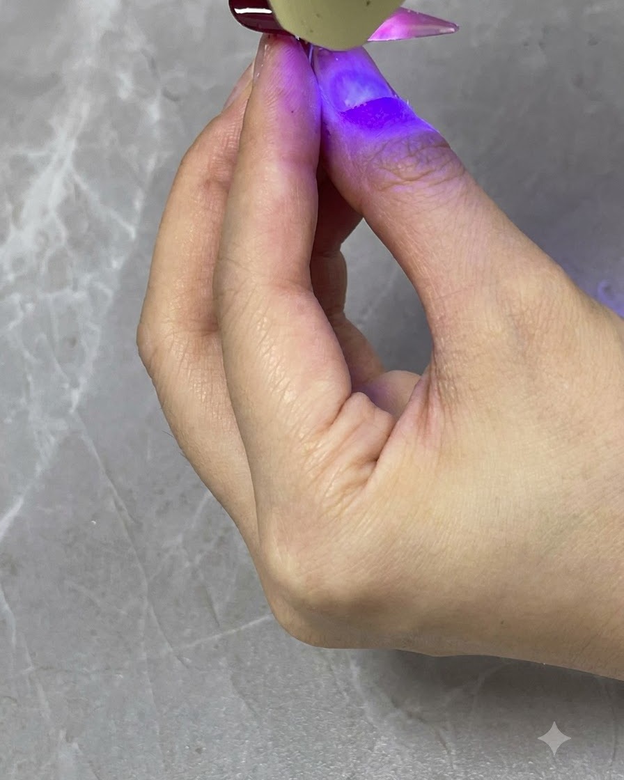 Una lampada UV/LED portatile che polimerizza uno strato di sfumatura rosso traslucido su ununghia finita.