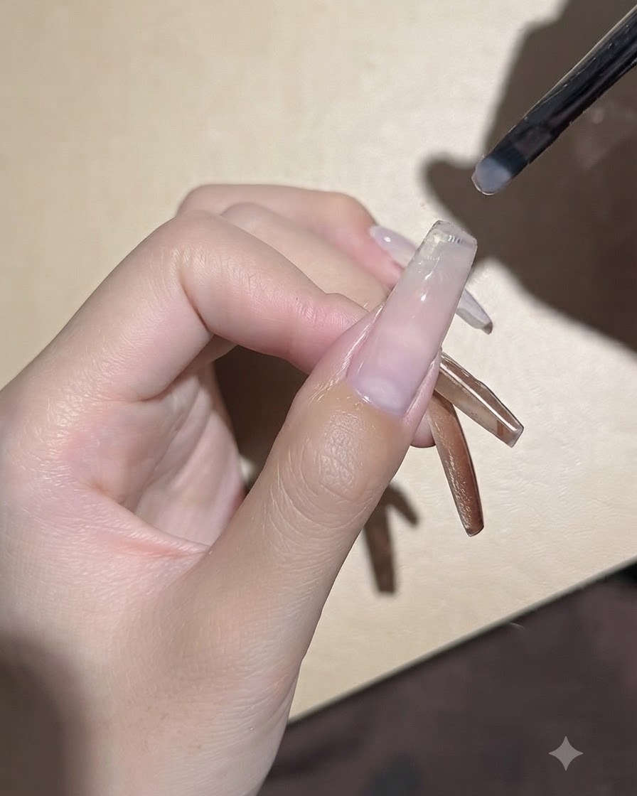 Un piccolo pennello da gel applica un sottile strato uniforme di gel base trasparente su una piastra ungueale allungata.