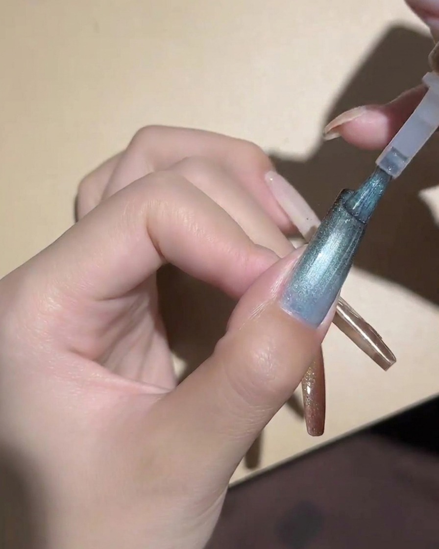 Un magnete cilindrico tenuto vicino a ununghia cat-eye blu per magnetizzare le particelle.