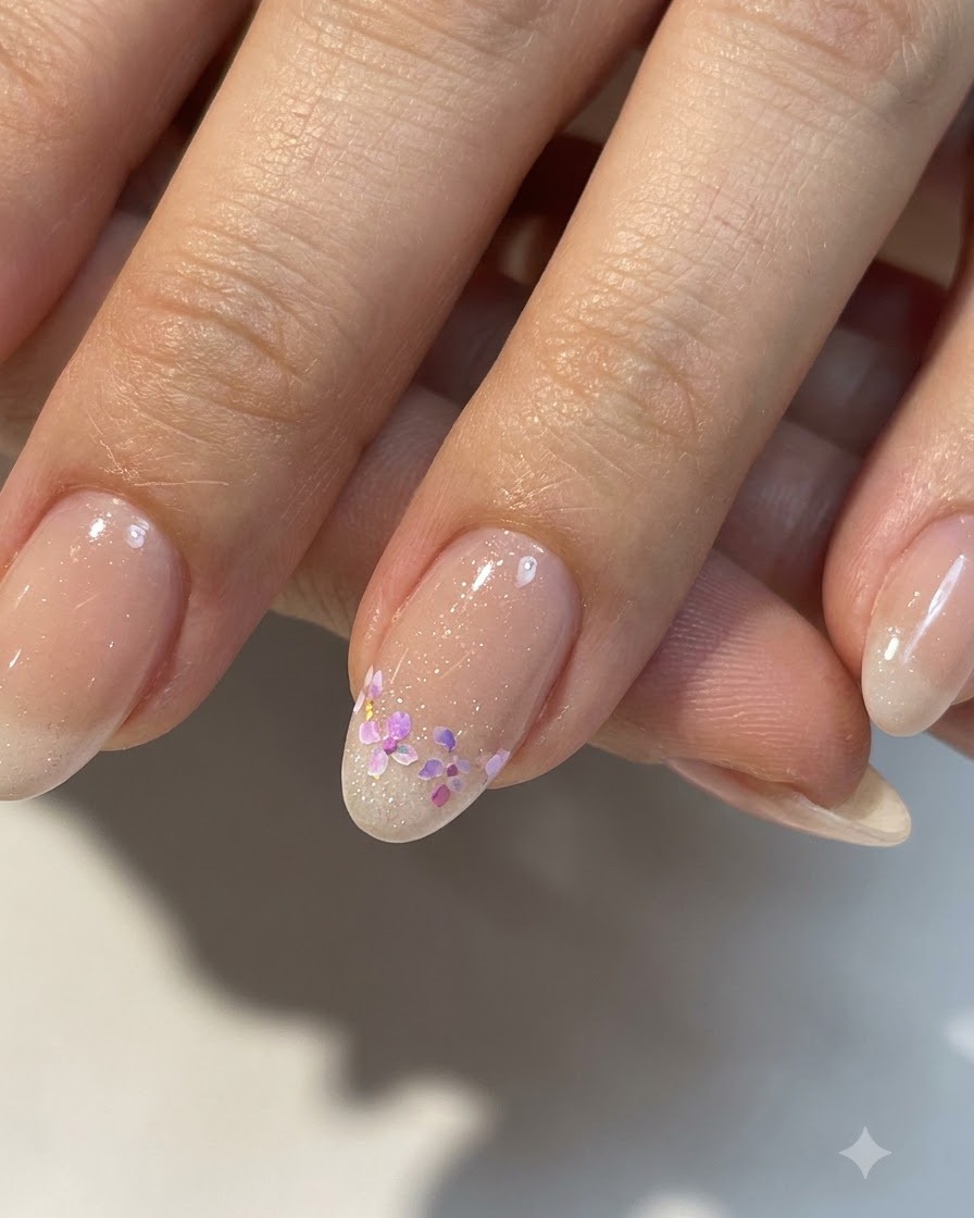Un primo piano di una piccola nail art floreale completata su una base nude lucida con dettagli rifiniti.
