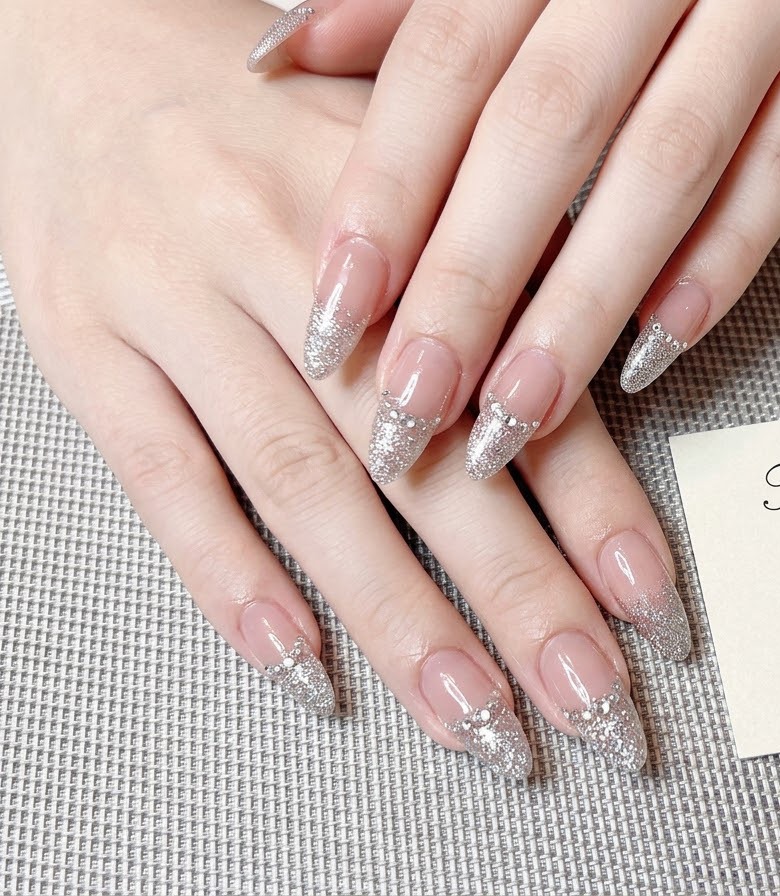 Dita con punte French glitterate che riflettono intensamente la luce sotto illuminazione da studio.