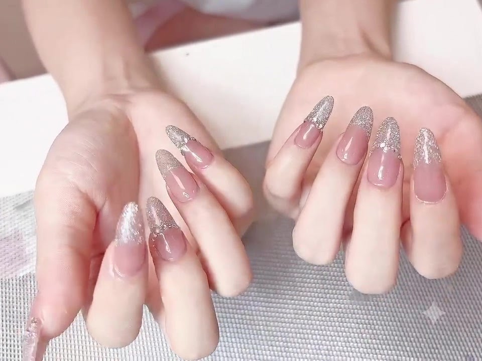 Due mani con unghie finite a base rosa nude e punte French con glitter argento, che mettono in risalto la struttura liscia e lucida del top coat.