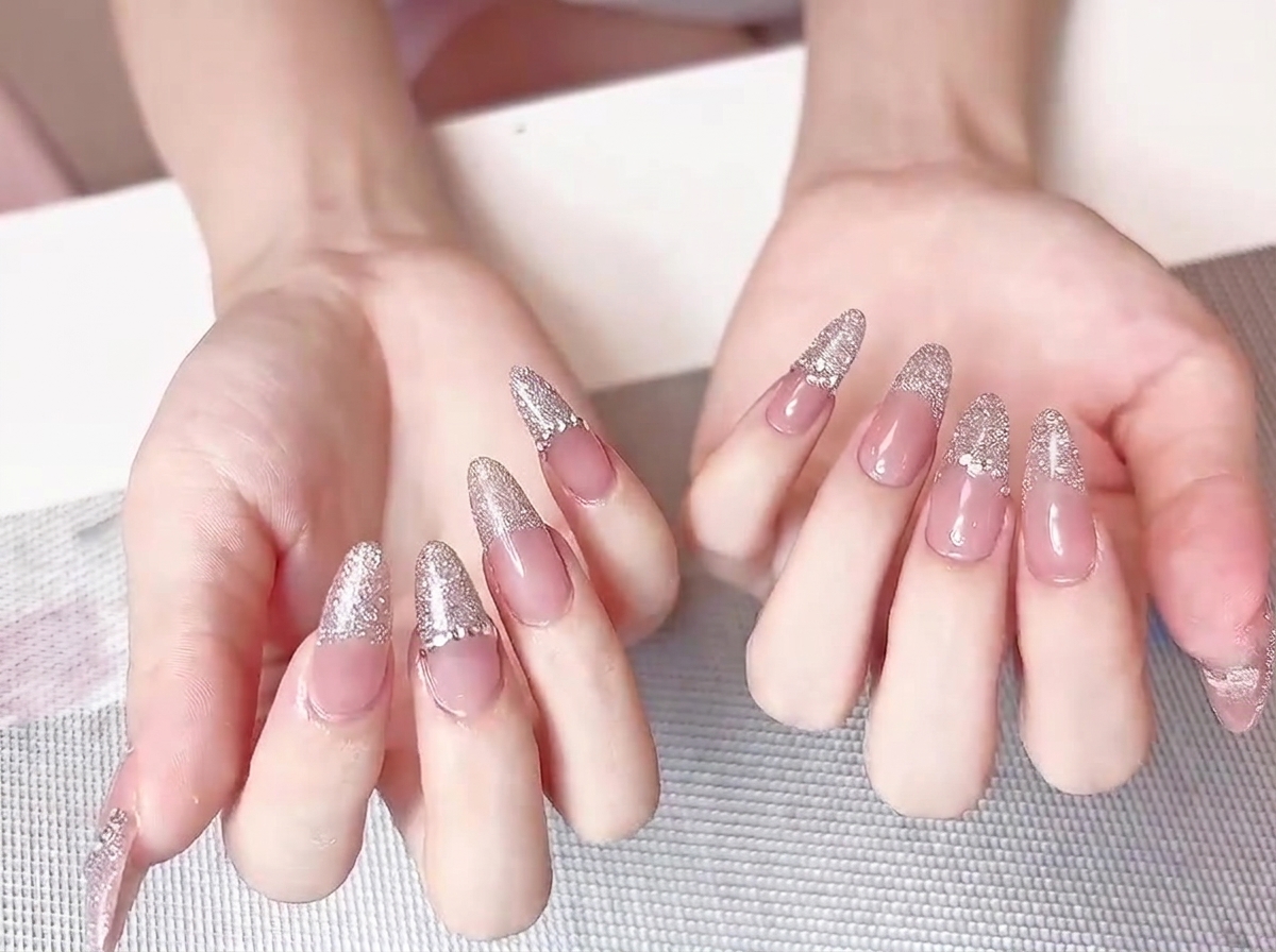 Dita unite che mostrano un set completo di unghie con French nude e glitter argento rifinite con eleganza.