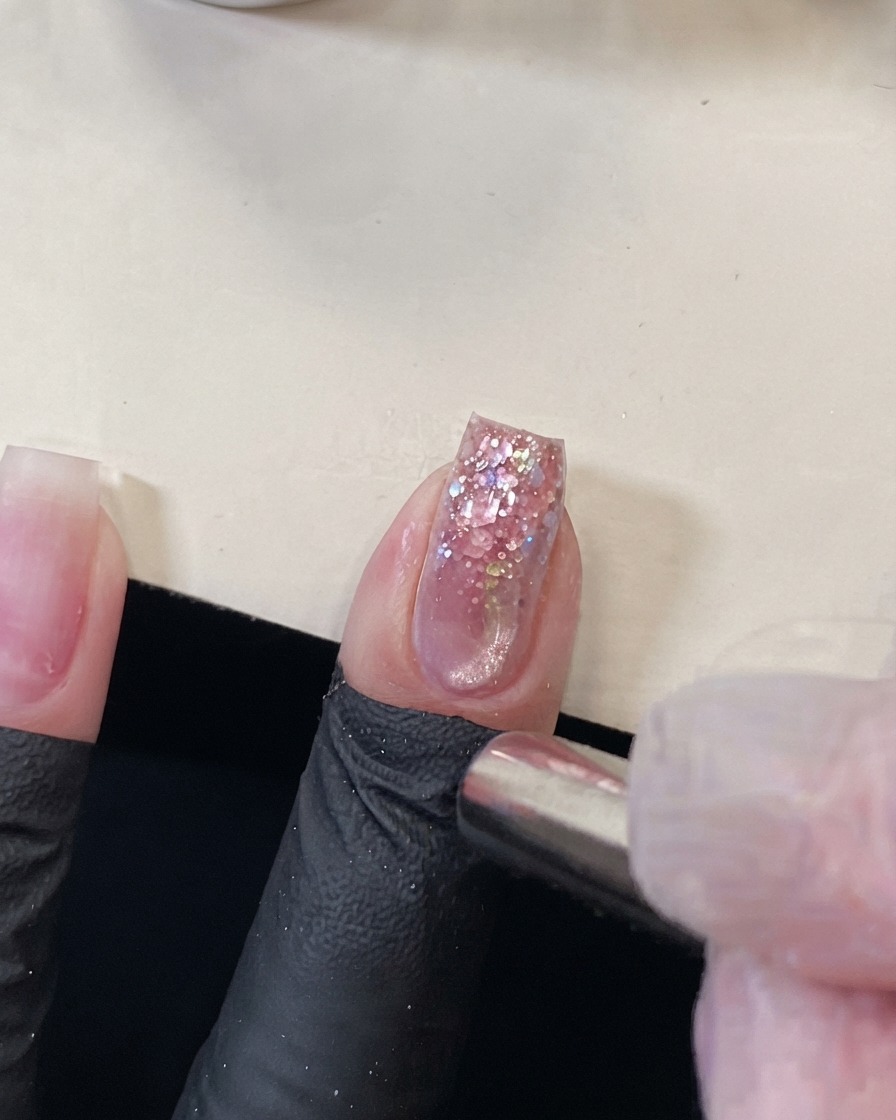 Un magnete cilindrico tenuto vicino alla punta di ununghia glitterata rosa per spingere leffetto cat eye magnetico.