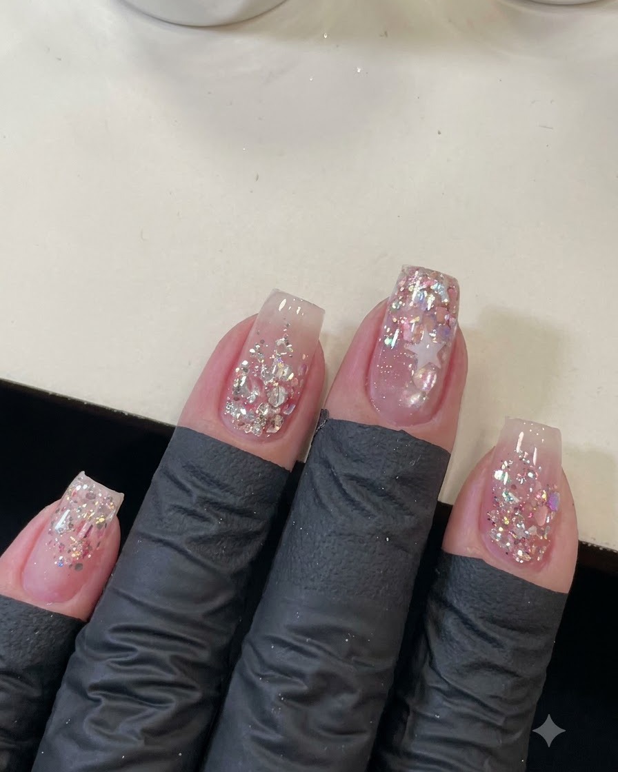 Una ripresa dallalto di quattro unghie curate decorate con sequins rosa scintillanti e il contorno di una stella.