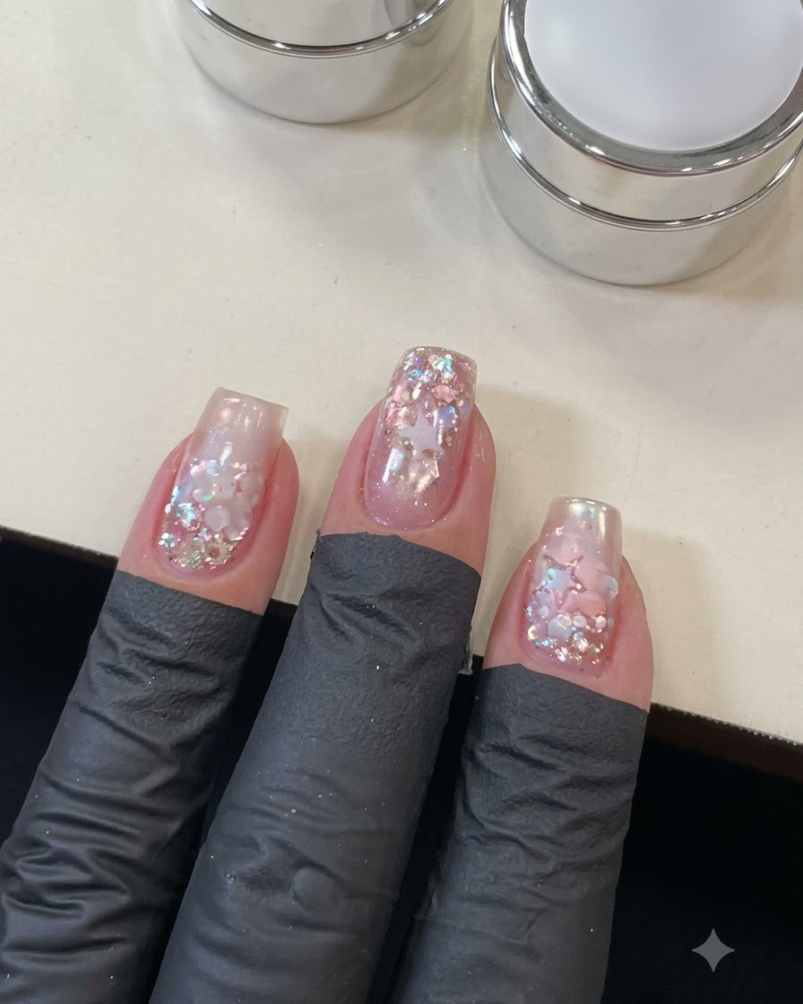 Una vista ravvicinata di una mano che applica il top coat sulla dettagliata nail art con stelle e sequins.