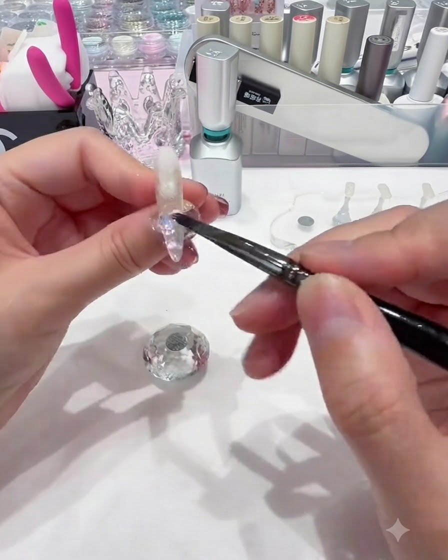Un piccolo pennello da unghie che deposita paillettes circolari colorate sul gel base bagnato vicino alla base dellunghia.