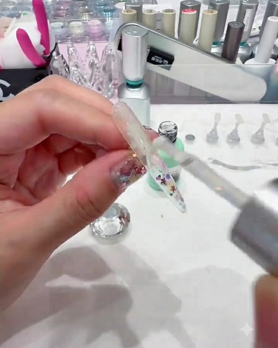 Un pennello che applica uno strato spesso di builder gel trasparente su ununghia decorata con paillettes per incapsularla senza intoppi.