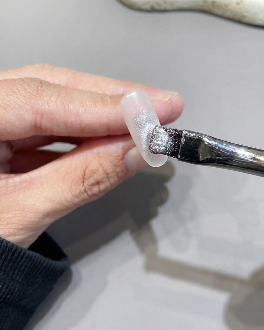 Un pennello piatto che stende il gel cat eye argento scintillante sulla superficie dellunghia.