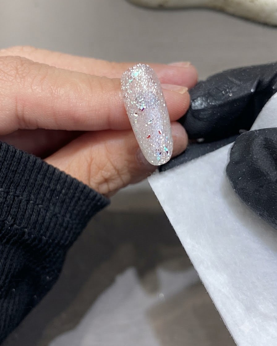 Una mano guantata con un pad di cellulosa accanto alla superficie dellunghia brillante appena polimerizzata.