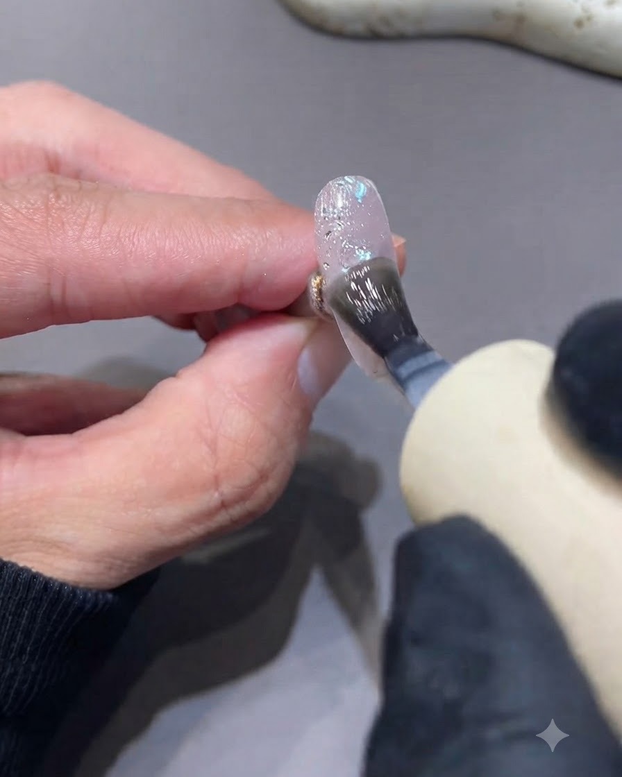 Un pennello che stende un top coat opaco sopra ununghia texturizzata con glitter e scaglie.