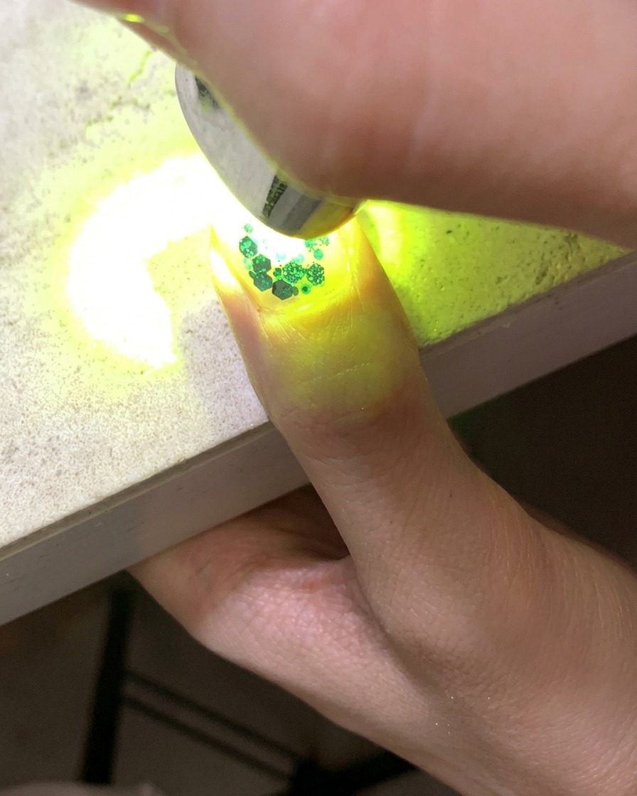 Una mini lampada UV che polimerizza ununghia decorata con glitter e paillettes a stella cava.
