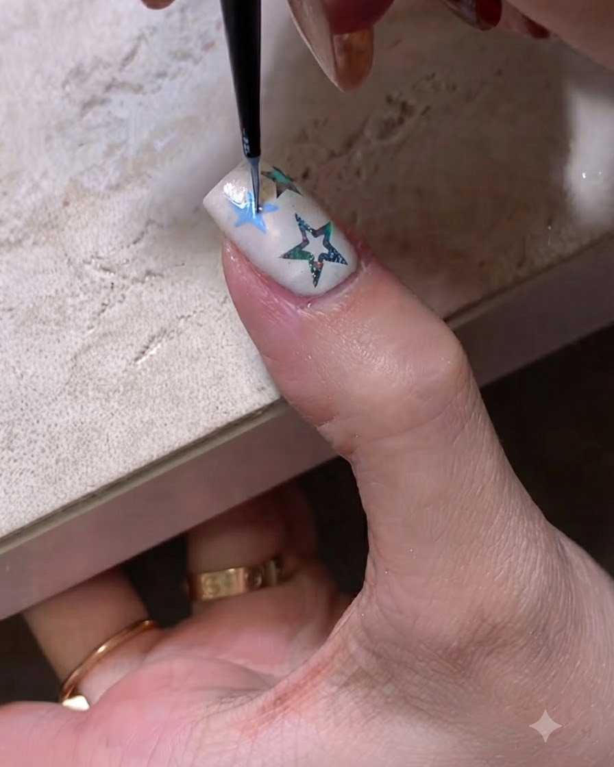 Primo piano di un pennello fine per nail art che disegna il contorno di una stella blu su ununghia curata.