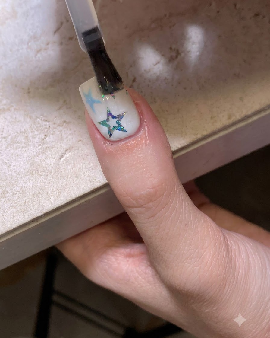Un pennello che applica un top coat trasparente lucido su ununghia decorata con stelle e glitter.