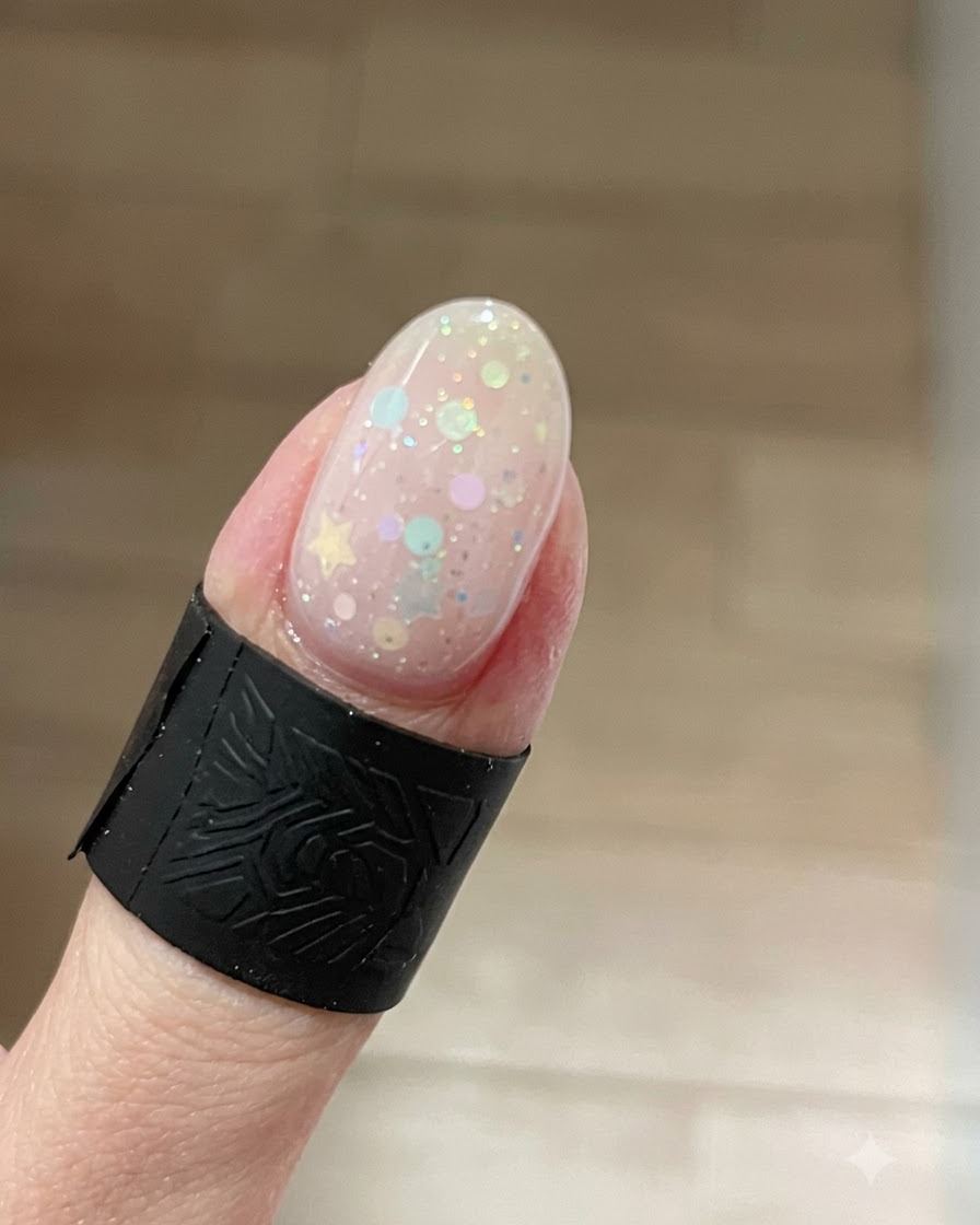 Un primo piano di ununghia che mostra un brillante effetto gel cat-eye con glitter concentrati sulla punta sopra i glitter a stella.