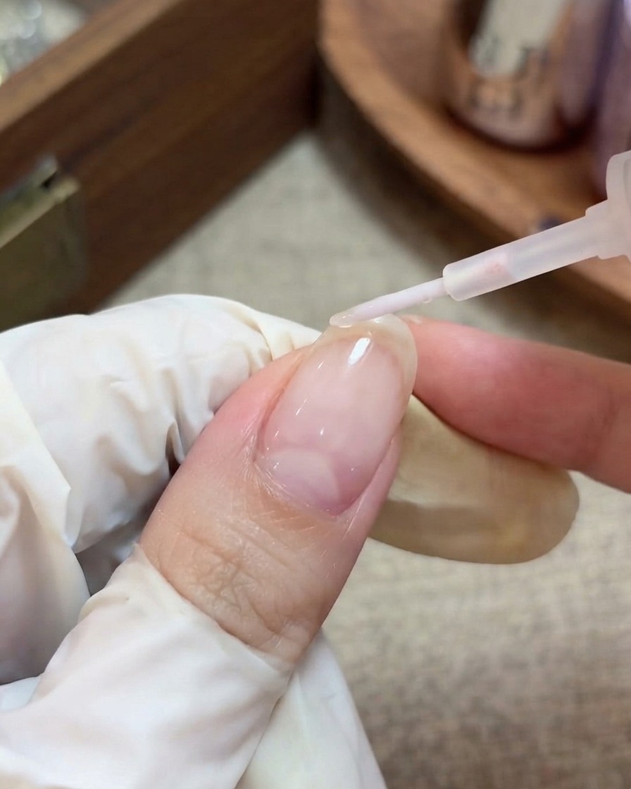 Una mano con i guanti che usa un pennello per applicare un top coat trasparente e lucido su ununghia preparata con glitter a stella incapsulati.
