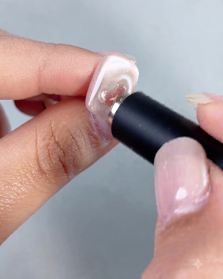 Uno strumento magnetico cilindrico tenuto vicino a ununghia, che concentra i riflessi allinterno di un piccolo cuore cat-eye dipinto.