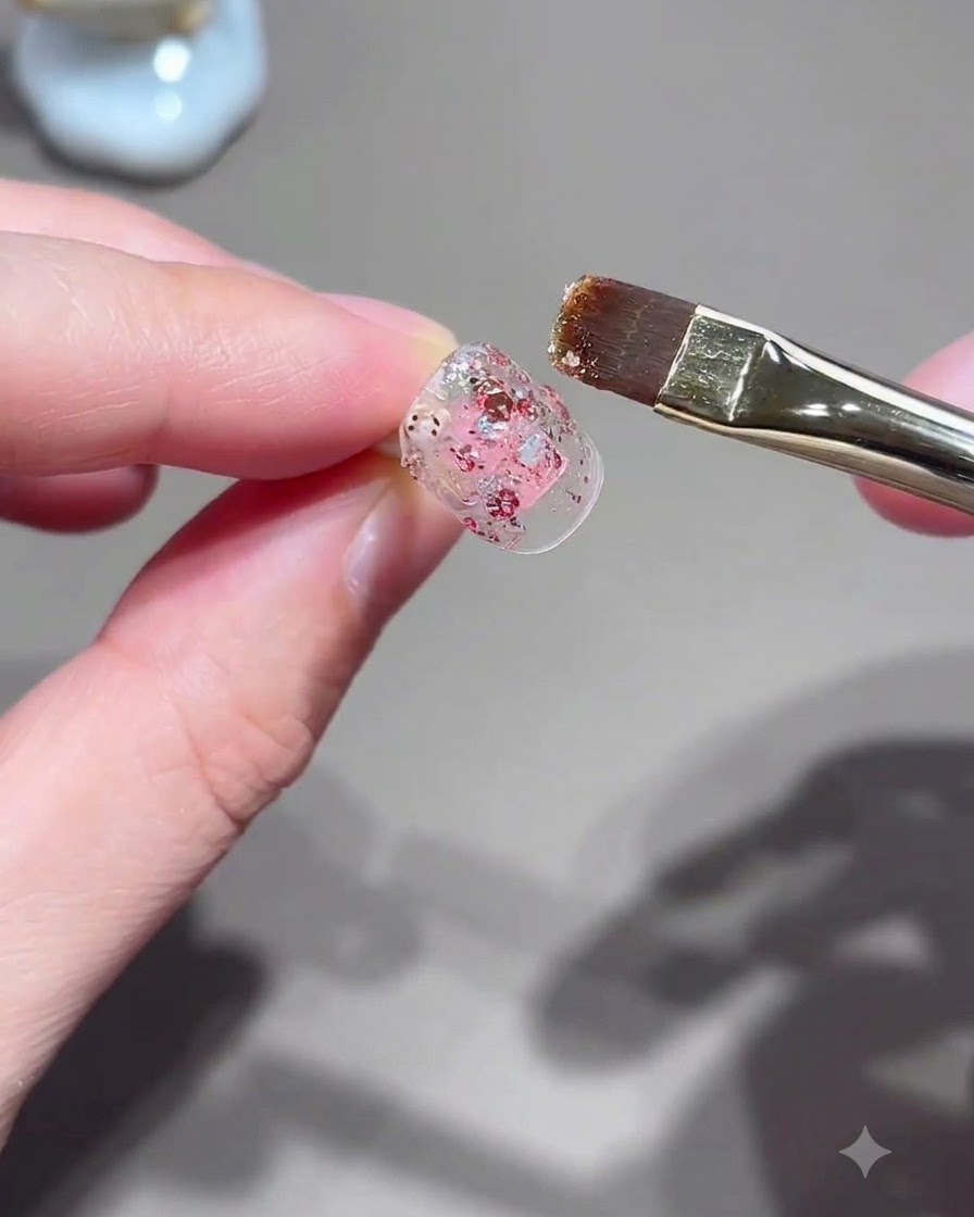 Un pennello piatto per unghie applica il gel glitterato rosa su una tip.