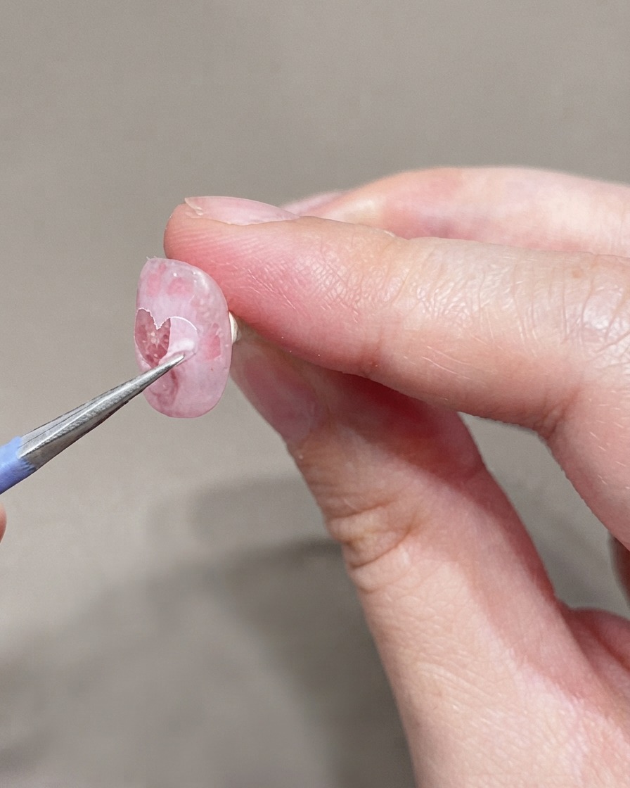 Un pennello sottile applica un secondo strato di smalto gel rosa molto chiaro sullunghia preparata.