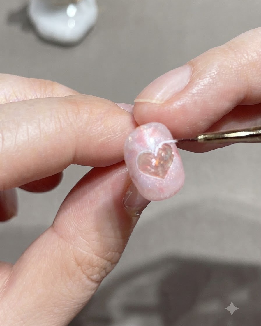Un pennello liner fine traccia il bordo esterno di un adesivo a cuore su ununghia in gel rosa.