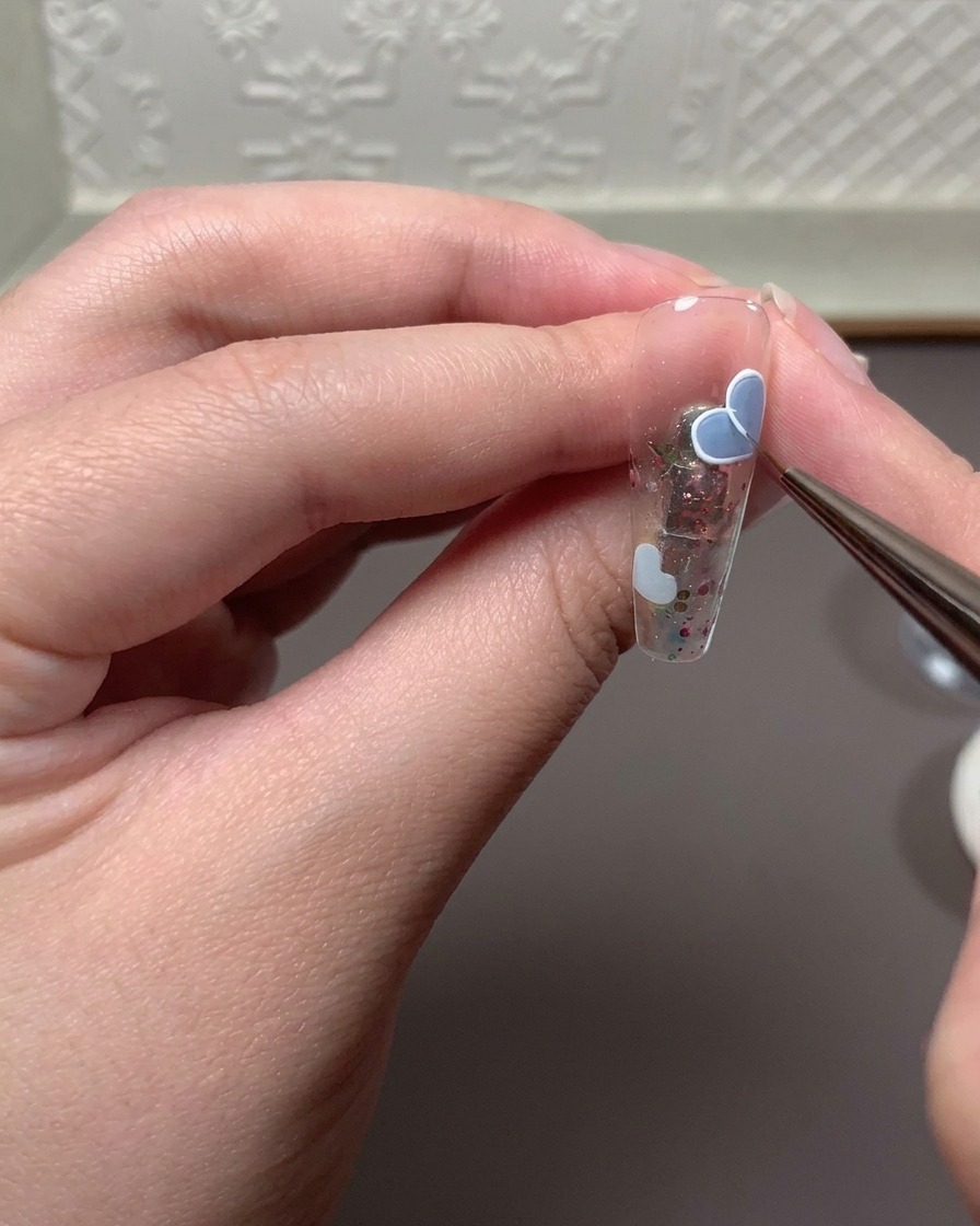 Un pennello fine che applica una miscela di gel da rilievo e gel da disegno bianco per tracciare il contorno di un cuore.