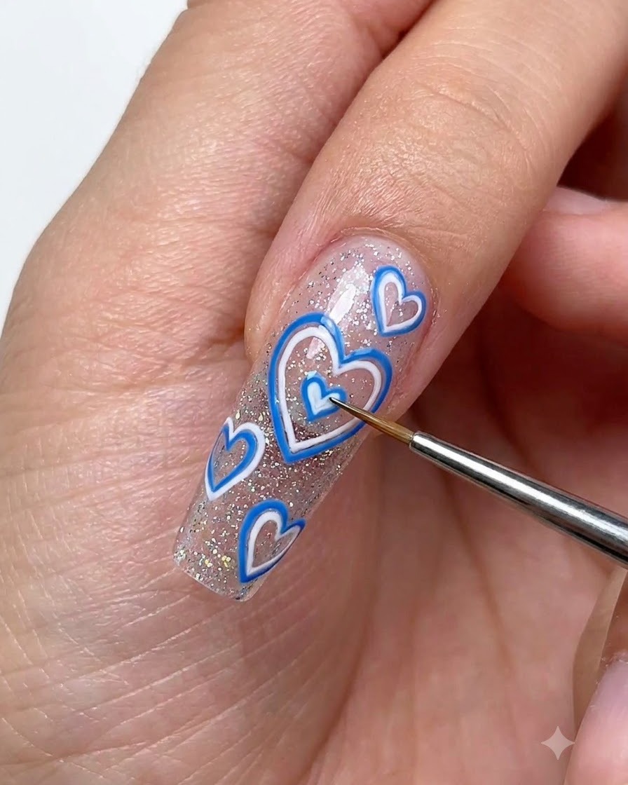 Un pennello di dettaglio fine che utilizza gel da disegno bianco per delineare piccoli cuori dimensionali su ununghia estesa e scintillante.