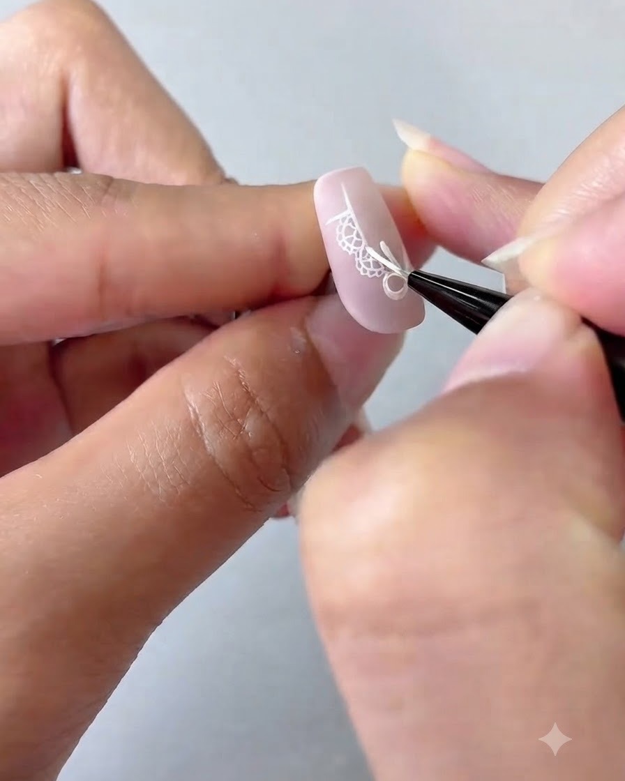 Un pennello da nail art che aggiunge dettagli di punti bianchi e una stella a quattro punte su ununghia con sfumatura rosa.