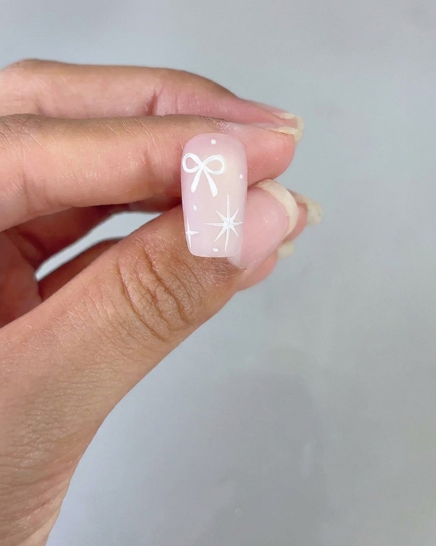 Un design di unghia finito con un fiocco bianco e una stella a quattro punte su base sfumata rosa mostrato per la visualizzazione.