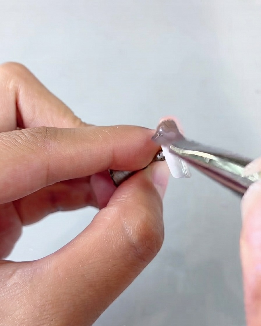 Un paio di pinzette che tengono una tip di unghia mentre applicano uno strato di gel cat eye.