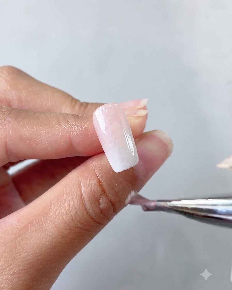 Una mano che tiene un pennello che applica una base coat in gel cat eye bianco latte su ununghia.