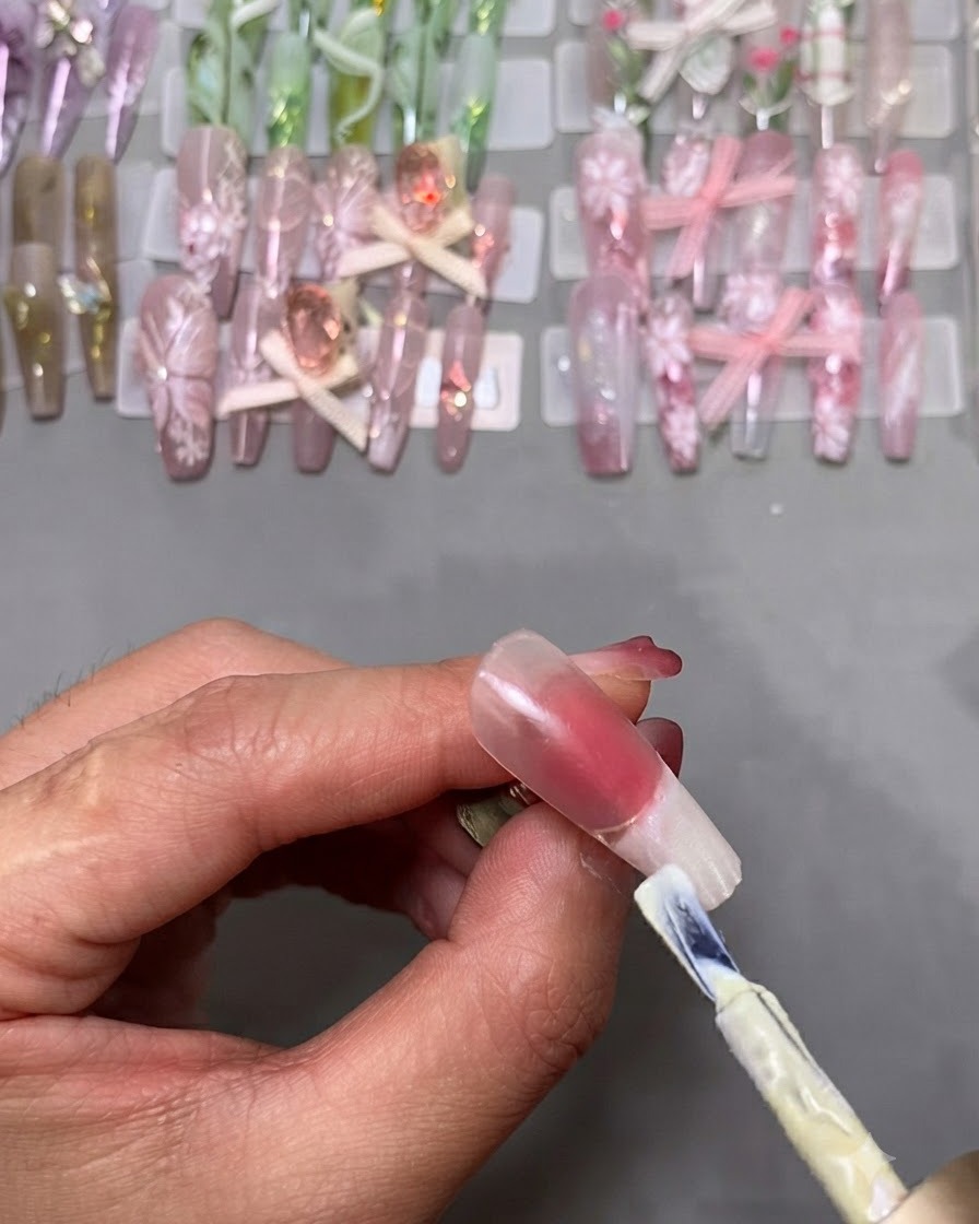Un pennello da smalto gel applica lo smalto bianco sulla punta di ununghia finta montata su un supporto.
