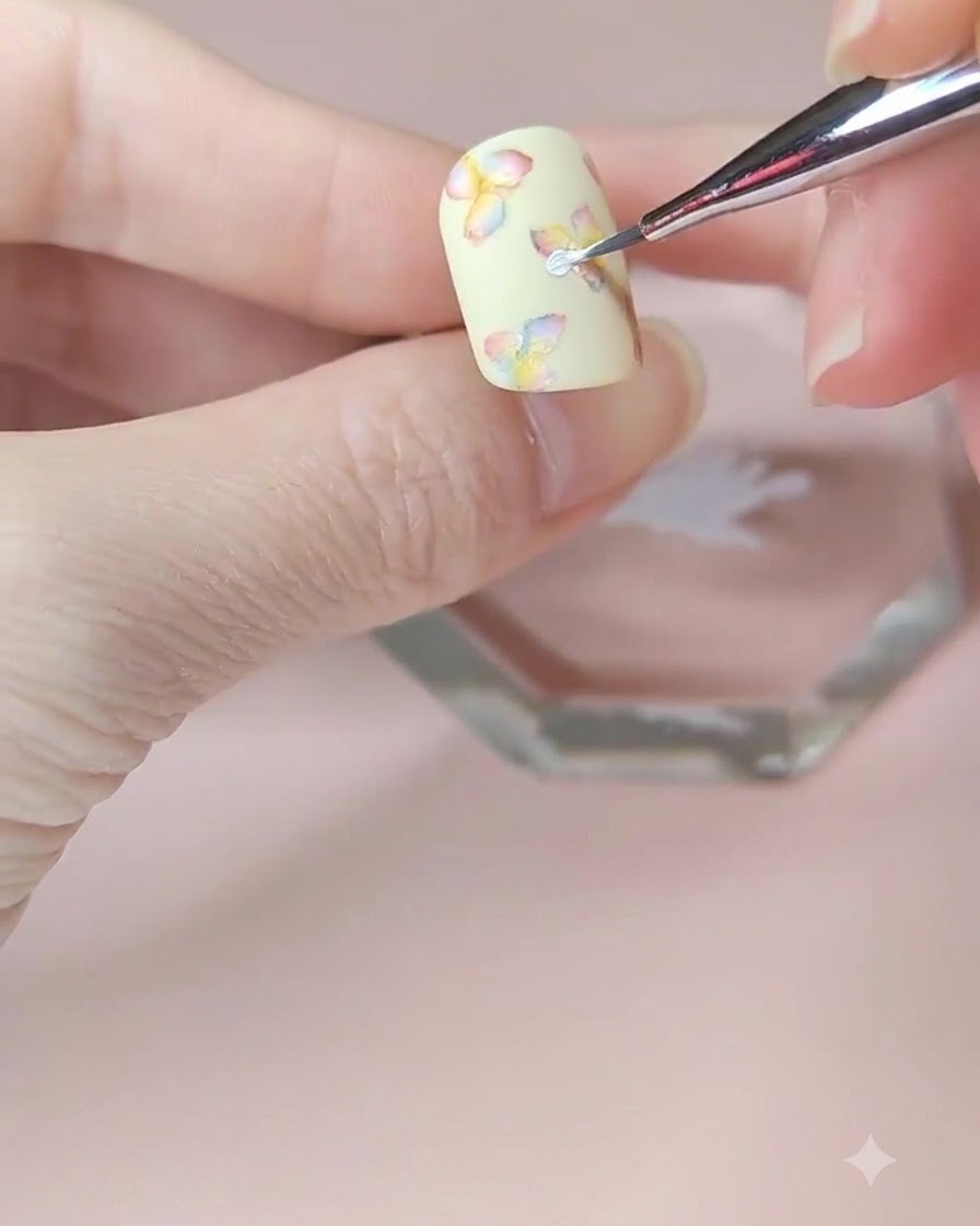Un primo piano dettagliato di un pennello da nail art che aggiunge un secondo strato di petali bianchi al fiore centrale.