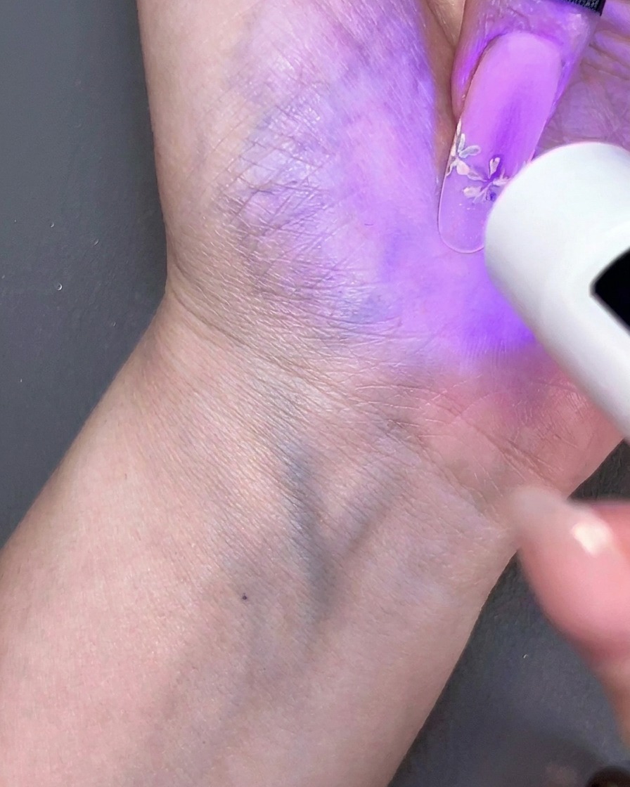 Una mini lampada UV portatile che polimerizza un design per unghie floreale sotto una luce viola.