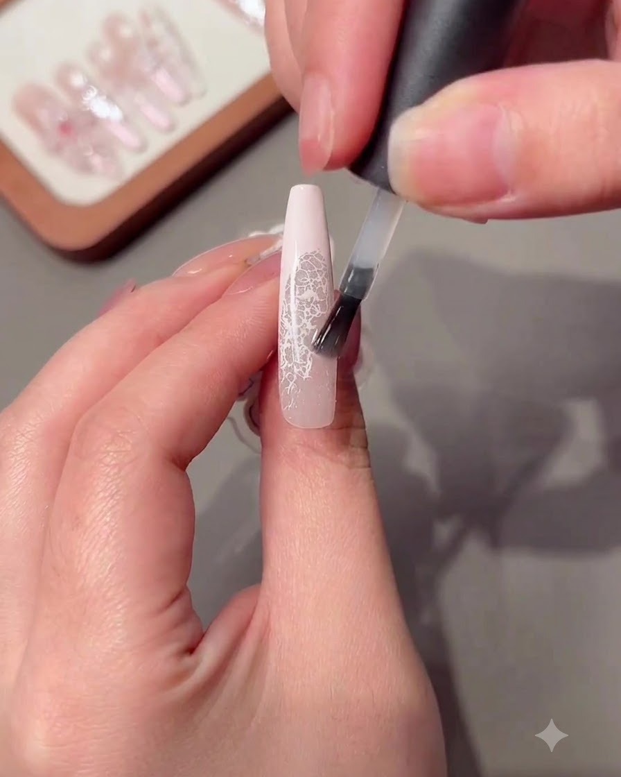Un pennello che applica uno strato trasparente di gel rinforzante su una lunga unghia decorata.