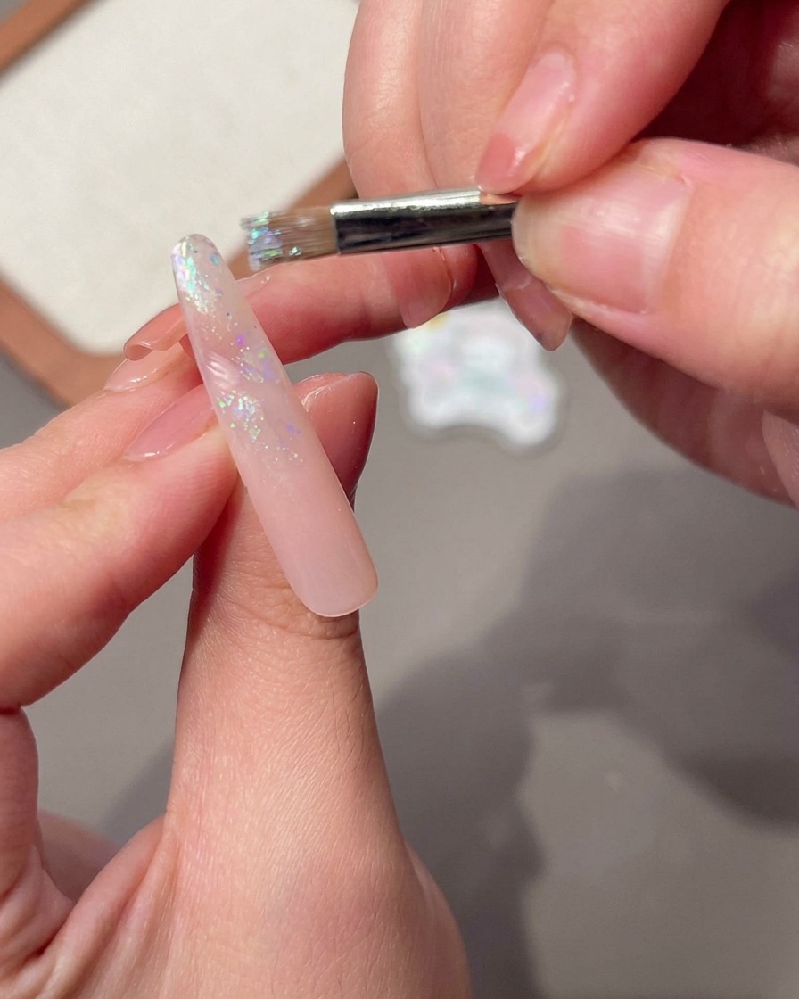 Un pennello che applica uno strato bagnato di gel di base su una lunga unghia rosa.