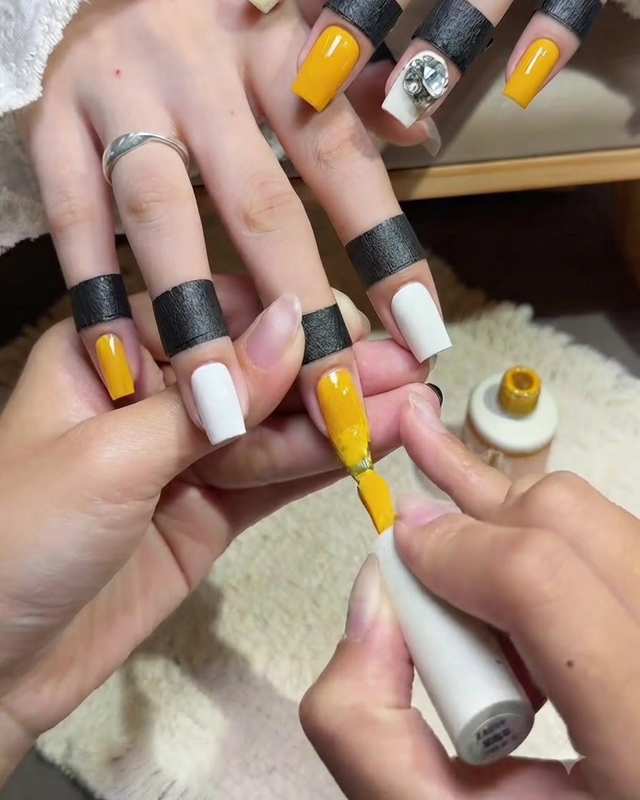 Primo piano di unonicotecnica che applica una seconda mano liscia di smalto gel giallo brillante sullunghia del dito indice con il pennello.