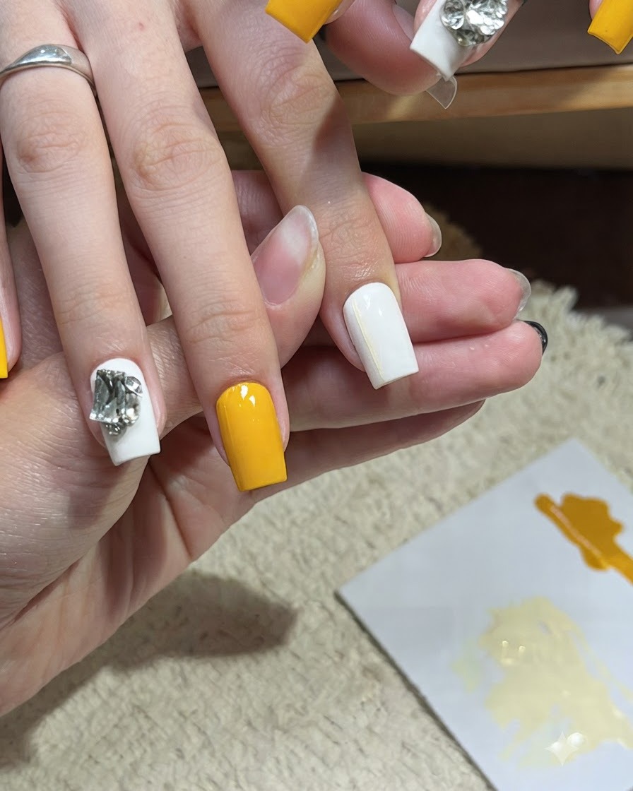 Un pennello per nail art che applica una seconda sottile linea orizzontale gialla su ununghia bianca.