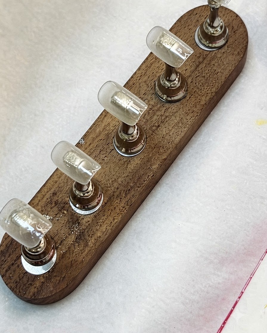Un pennello che applica la base coat trasparente sulle tip per unghie montate su un supporto in legno.