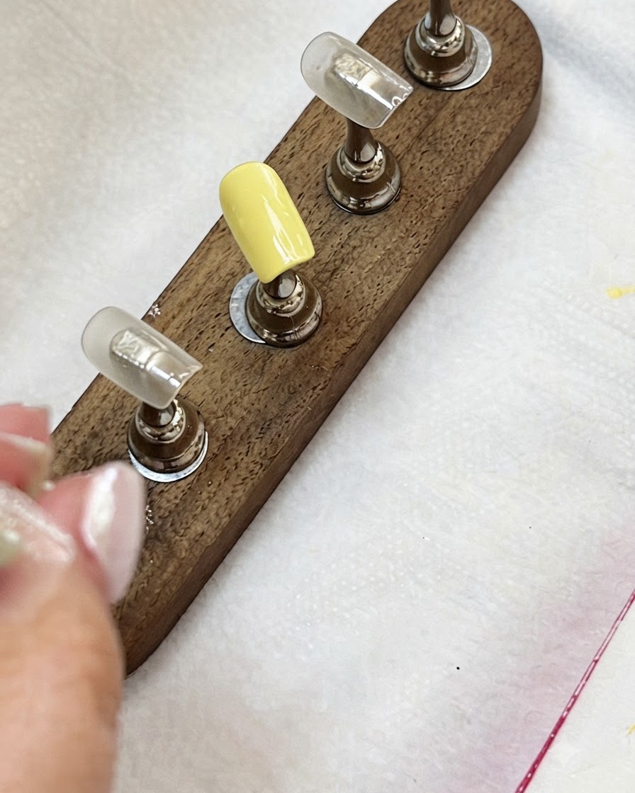 Tip per unghie su un supporto in legno che mostrano una tip giallo lattiginoso e tip color nudo.
