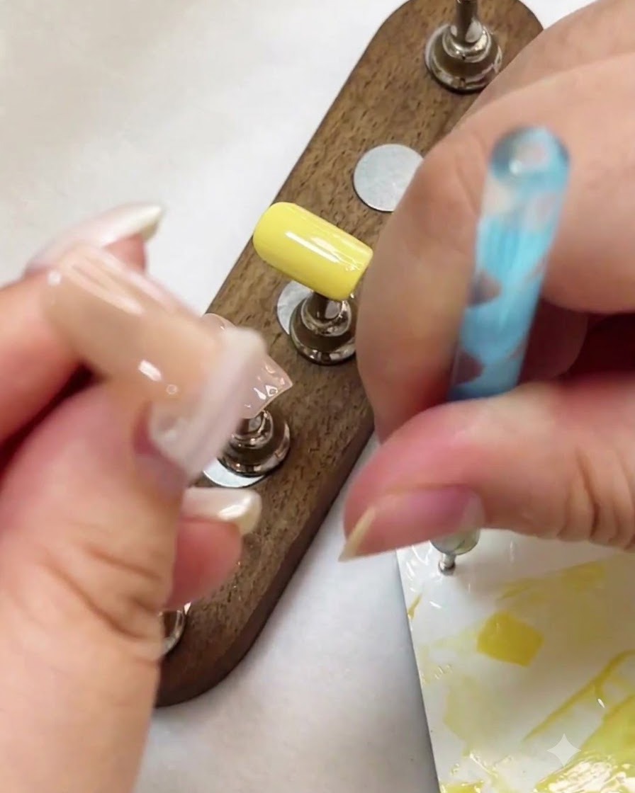 Una penna per dotting utilizzata per posizionare punti di gel bianco su una superficie dellunghia color nudo.