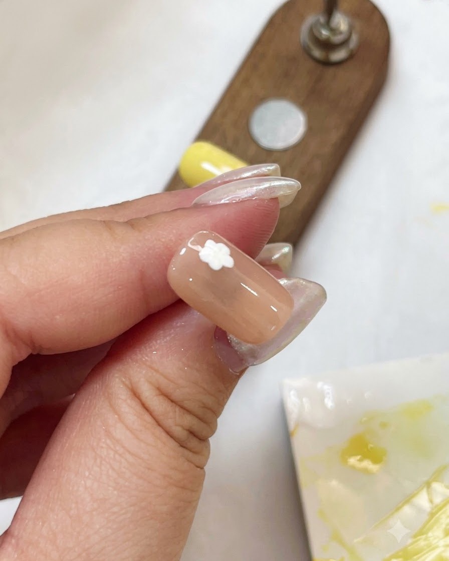 Primo piano di ununghia nuda con un design a petali di fiore bianco in fase di polimerizzazione tramite una piccola torcia a penna viola.