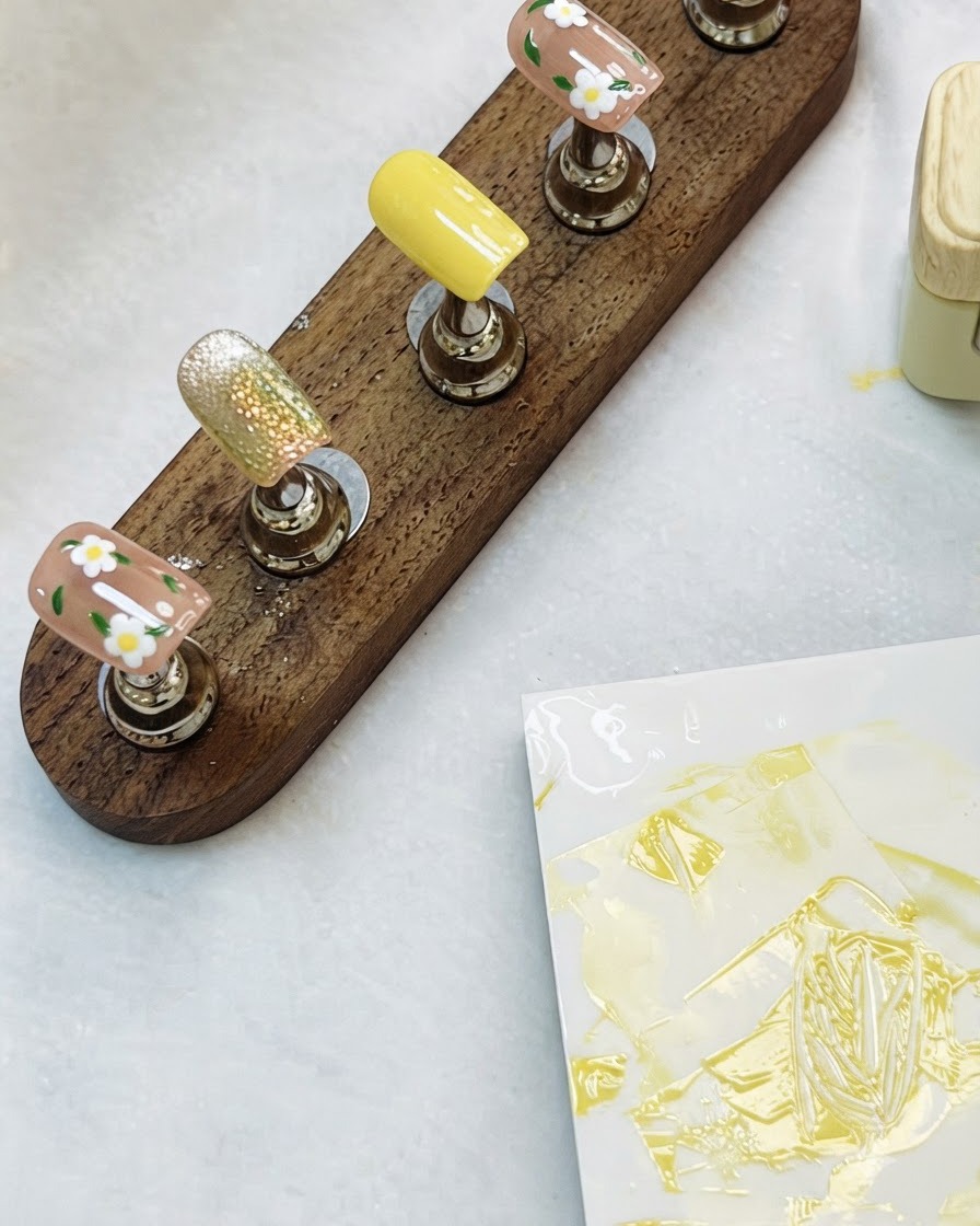 Un supporto da esposizione in legno che sostiene tip per nail art floreali e cat-eye completate su un tavolo.