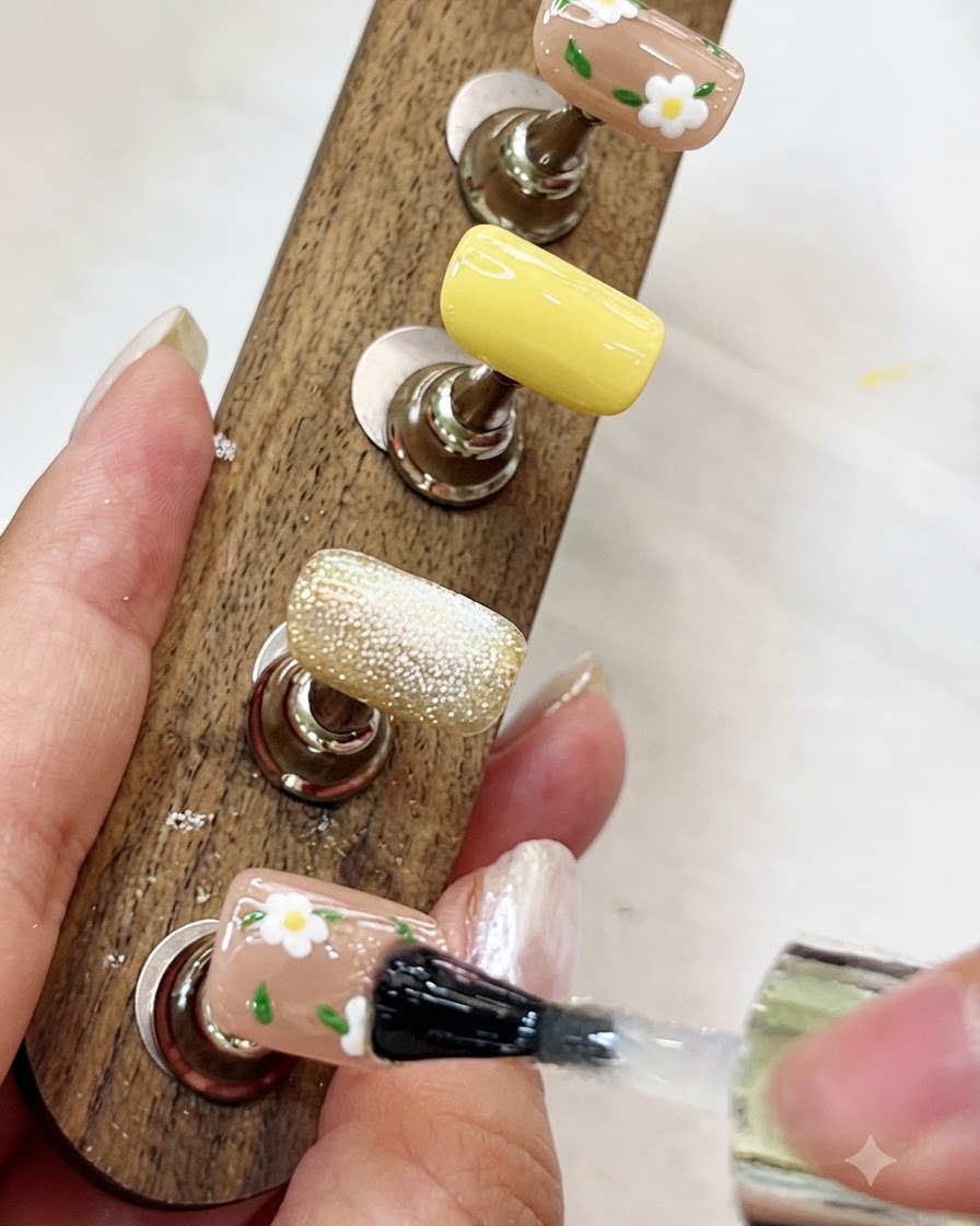 Un pennello che applica un top coat lucido trasparente su ununghia dipinta con fiori su un supporto da esposizione in legno.
