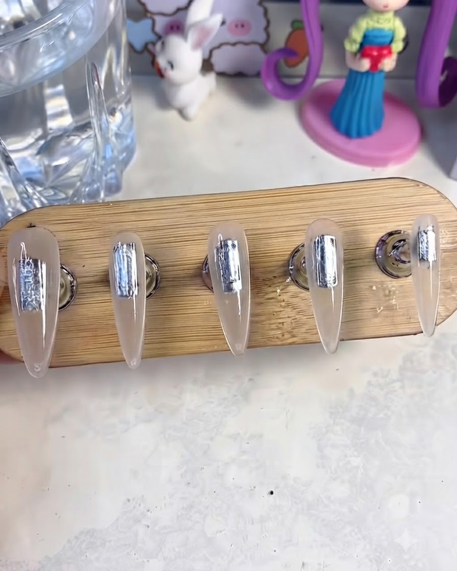 Un supporto per unghie con cinque unghie finte posizionate allinterno di una lampada UV/LED per polimerizzare lo strato di base gel.